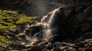 The sun rays shine on a mountain waterfall